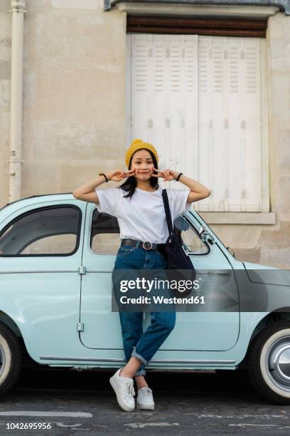 portrait of young woman standing at small car - vintage jeans stock pictures, royalty-free photos & images