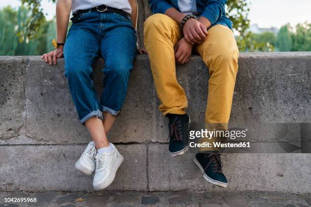 legs of a couple sitting on a wall - blue pants stock-fotos und bilder