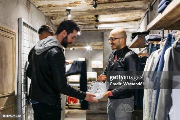 designer in modern menswear shop showing new shoes to man - smart shoes stock pictures, royalty-free photos & images