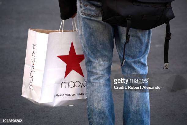 Man carrying a Macy's department store shopping bag waits at an intersection in San Francisco, California.