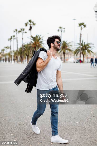 spain, barcelona, young man walking on promenade with palms - leather shirt fotografías e imágenes de stock