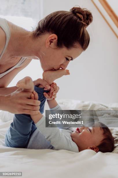 mother cuddling with her baby son - feet in bed stock-fotos und bilder