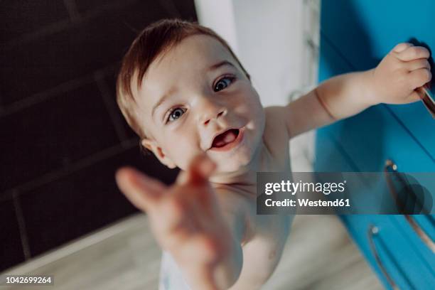 laughing baby boy holding on to chest of drawers, reaching up - baby standing stock pictures, royalty-free photos & images