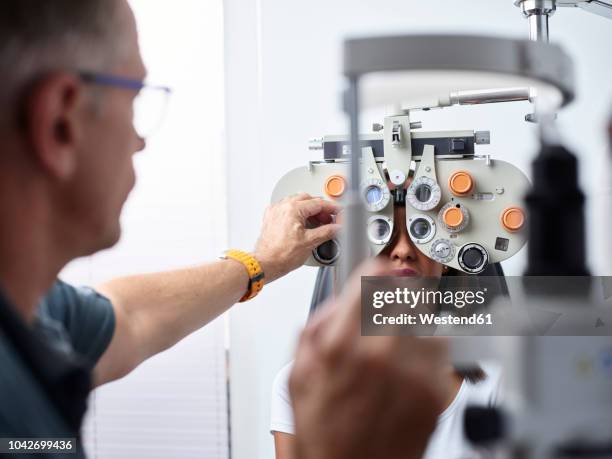 optometrist examining young woman's eye - optiker stock-fotos und bilder