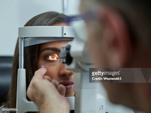 optometrist examining young woman's eye, contact lens on index finger - lente a contatto foto e immagini stock