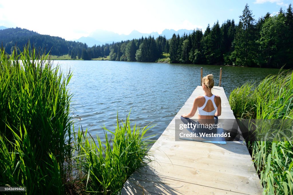 Germany, Mittenwald, back view of woman practising yoga on jetty at lake