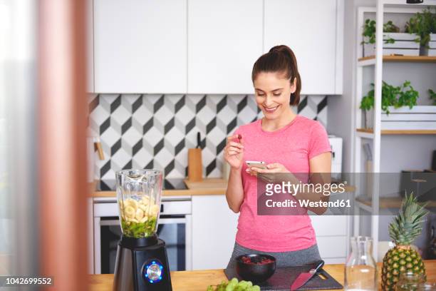 smiling young woman looking at cell phone in the kitchen - banana phone stock pictures, royalty-free photos & images