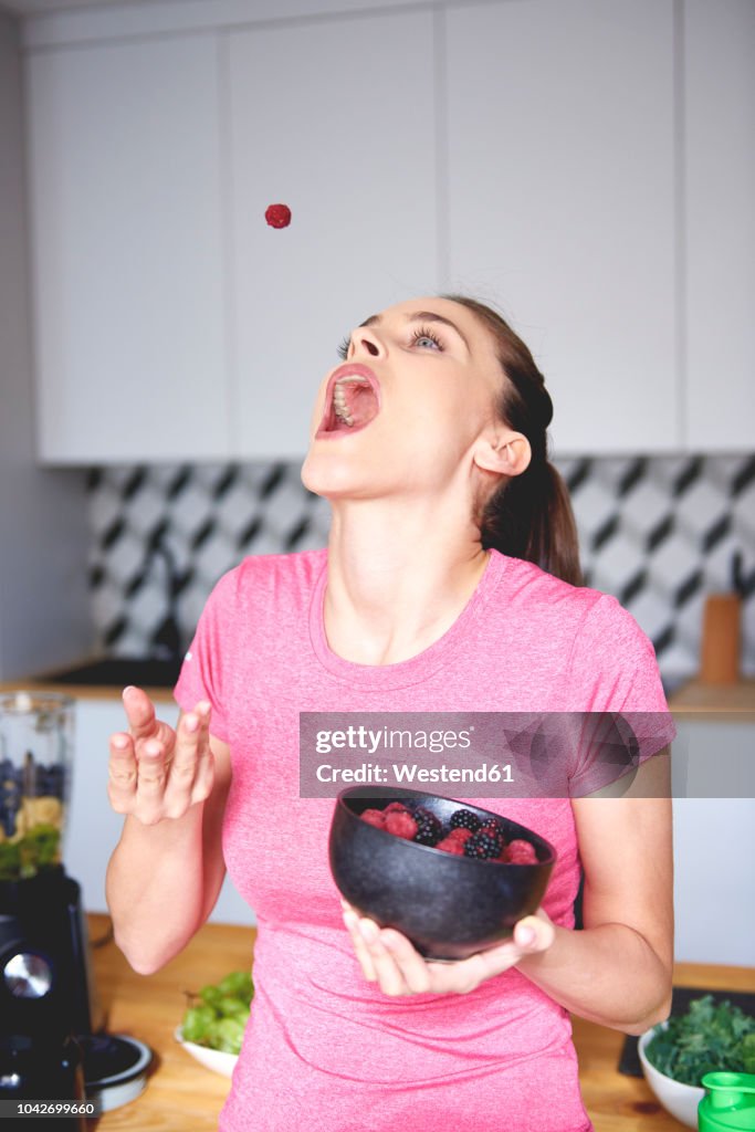 Young woman throwing raspberry in the air in the kitchen