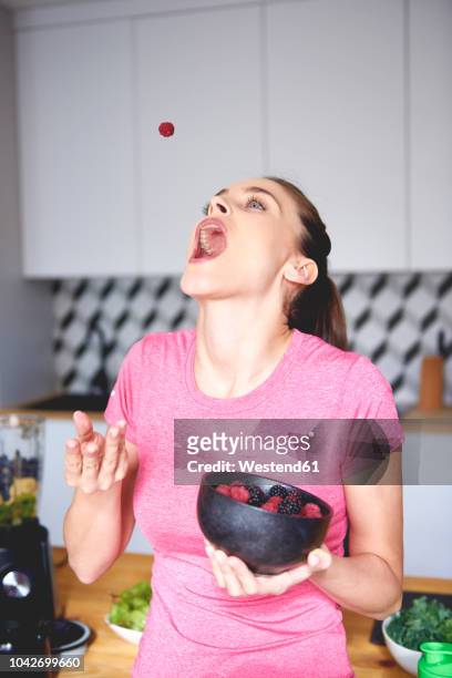 young woman throwing raspberry in the air in the kitchen - catch stockfoto's en -beelden