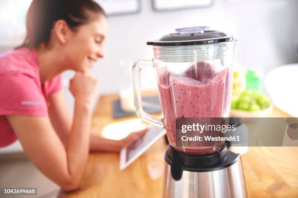 young woman using tablet in the kitchen while preparing smoothie - blender foto e immagini stock