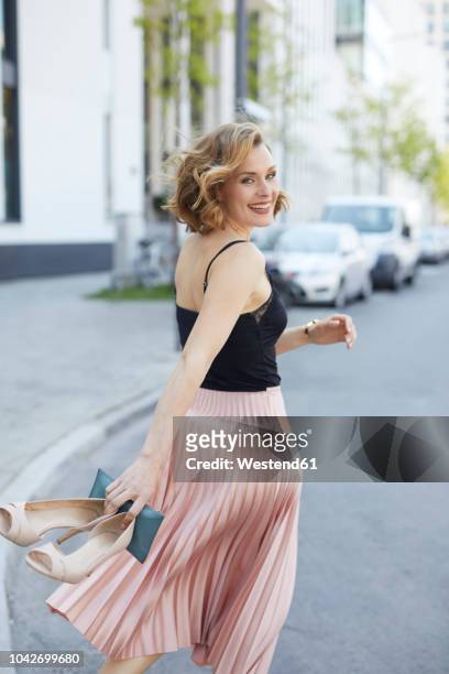 portrait of laughing woman with high heels and clutch bag in her hand walking on the street - höga klackar bildbanksfoton och bilder