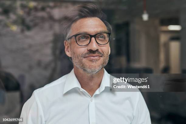 portrait of smiling man with stubble behind windowpane wearing white shirt and glasses - daydreaming stock pictures, royalty-free photos & images