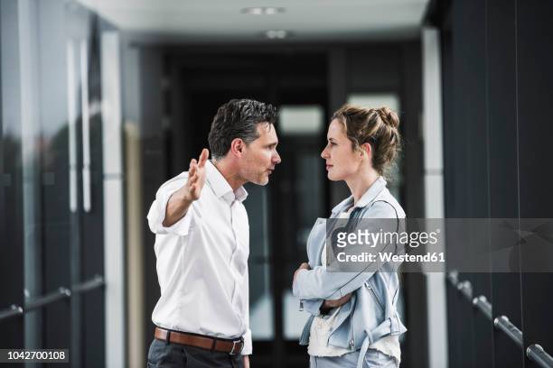 businesswoman and businessman arguing in office passageway - debate fotografías e imágenes de stock