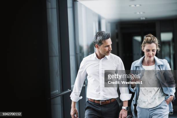 businesswoman and businessman talking in office passageway - business man walking photos et images de collection