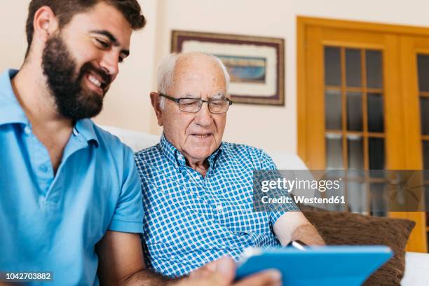 adult grandson teaching his grandfather to use tablet - pensioners demonstrate in spain stock pictures, royalty-free photos & images