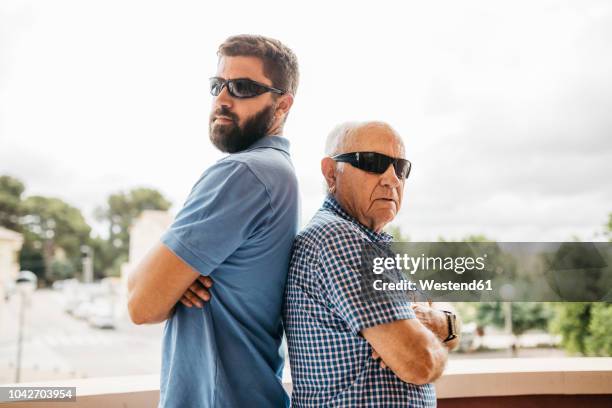 portrait of adult grandson and his grandfather wearing sunglasses standing back to back on balcony - cooler opa stock-fotos und bilder