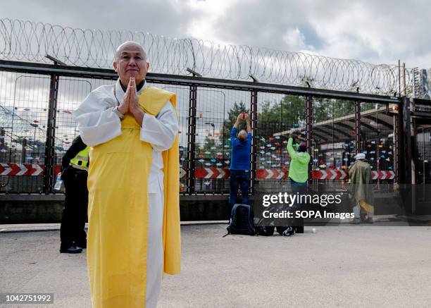 Monk is seen outside the North gate while protesters attach origami cranes to the gate in the background. Various members of different CND, Anti-war...