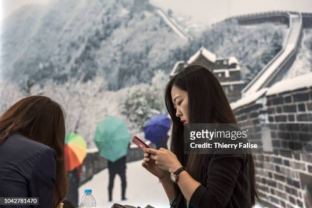 An Asian female participant reads her mobile phone under a poster of the Great Wall of China during the Annual Meeting of the New Champions of the...