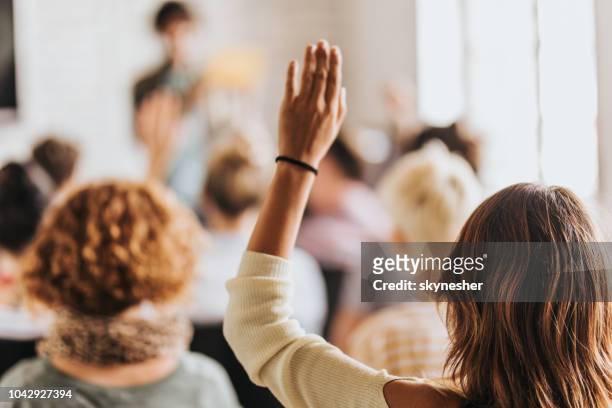 vista posteriore di una donna che alza il braccio in un seminario. - braccia alzate foto e immagini stock