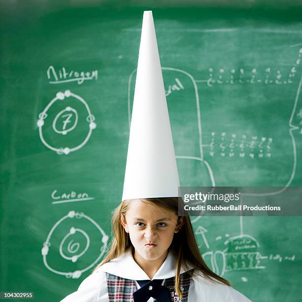 girl in a classroom standing in front of a chalkboard wearing a dunce cap - dumstrut bildbanksfoton och bilder