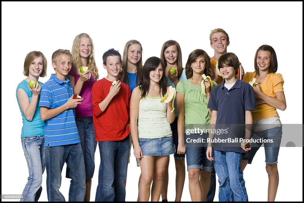 Teenagers holding pieces of fruit except for the girl in the middle with a cookie