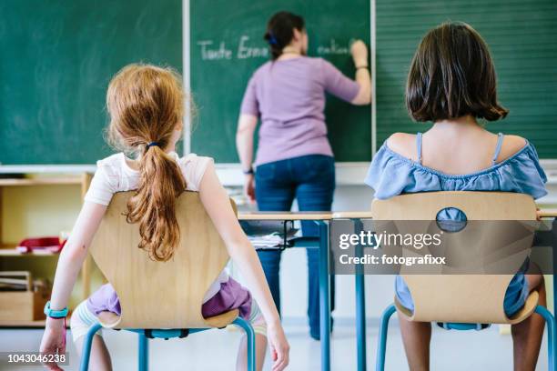 enseignante a écrit sur le tableau noir. vue arrière de deux jeunes filles à l’avant. - chaise de dos photos et images de collection