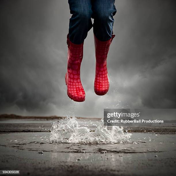 mujer joven con botas de goma salto en un charco, bajo la sección - black boot fotografías e imágenes de stock