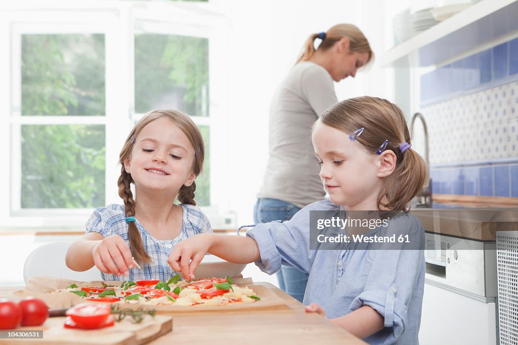 Germany, Munich, Girls (4-7) preparing food in kitchen, mother standing in background