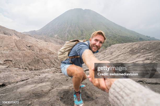 ung man fotvandring, drar ut handen för att nå en av lagkamrat. en hjälpande hand att nå toppen av kratern vulkanen. bromo vulkan regionen i indonesien, asien - climber hands bildbanksfoton och bilder