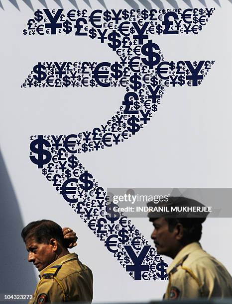 Indian policemen walk past a collage of the new Indian rupee symbol made with signs of the US dollar, the yen, the pound and the euro outside the...