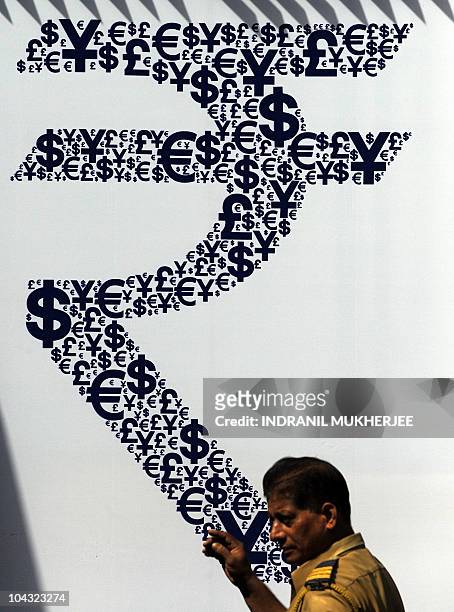 An Indian policeman walks past a collage of the new Indian rupee symbol made with signs of the US dollar, the yen, the pound and the euro outside the...