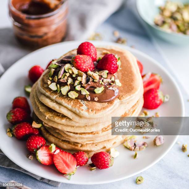 stack of pancakes with chocolate sauce, chopped pistachio nuts and strawberries - dutch pancakes stockfoto's en -beelden
