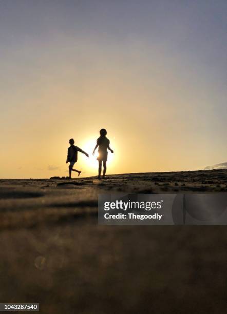 silhouette of a boy and girl running on the beach, fuerteventura, canary islands, spain - silhouette mädchen rennen stock-fotos und bilder