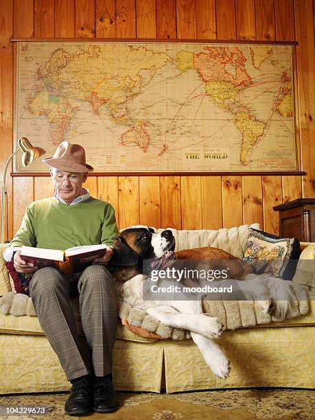 senior man sitting on sofa with dog, reading book - big world stock pictures, royalty-free photos & images