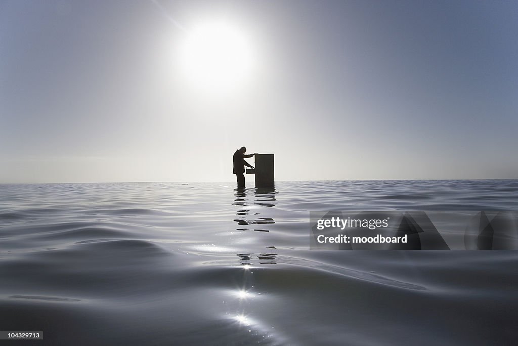 Silhouette of business man opening filing cabinet standing in middle os sea, side view