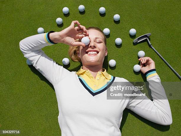 young female golfer lying on green, holding ball in front of eye, view from above - playing golf stock pictures, royalty-free photos & images