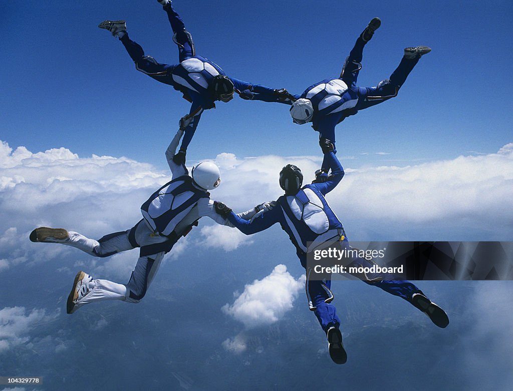 Four skydivers holding hands in ring against clouds