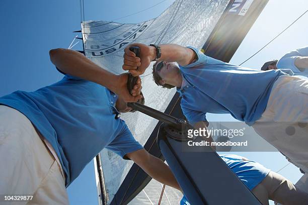 men raising sail on yacht, view from below - segeln stock-fotos und bilder