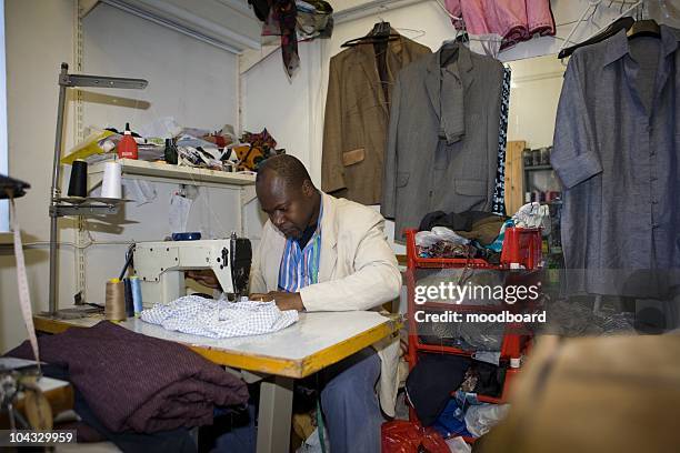 man sits at machine in textiles workshop - sweatshop stock pictures, royalty-free photos & images