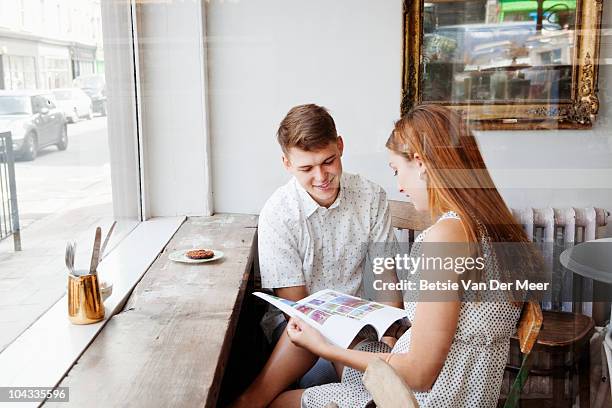 couple sitting in cafe looking at magazine. - boyfriend stock pictures, royalty-free photos & images