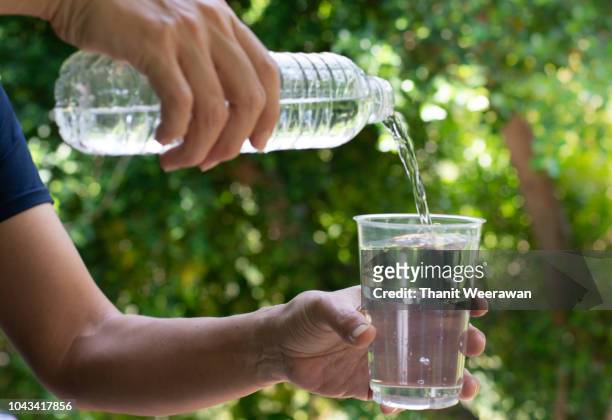 hand on pouring fresh water in the glass with the green nature background. - glass of water hand ストックフォトと画像