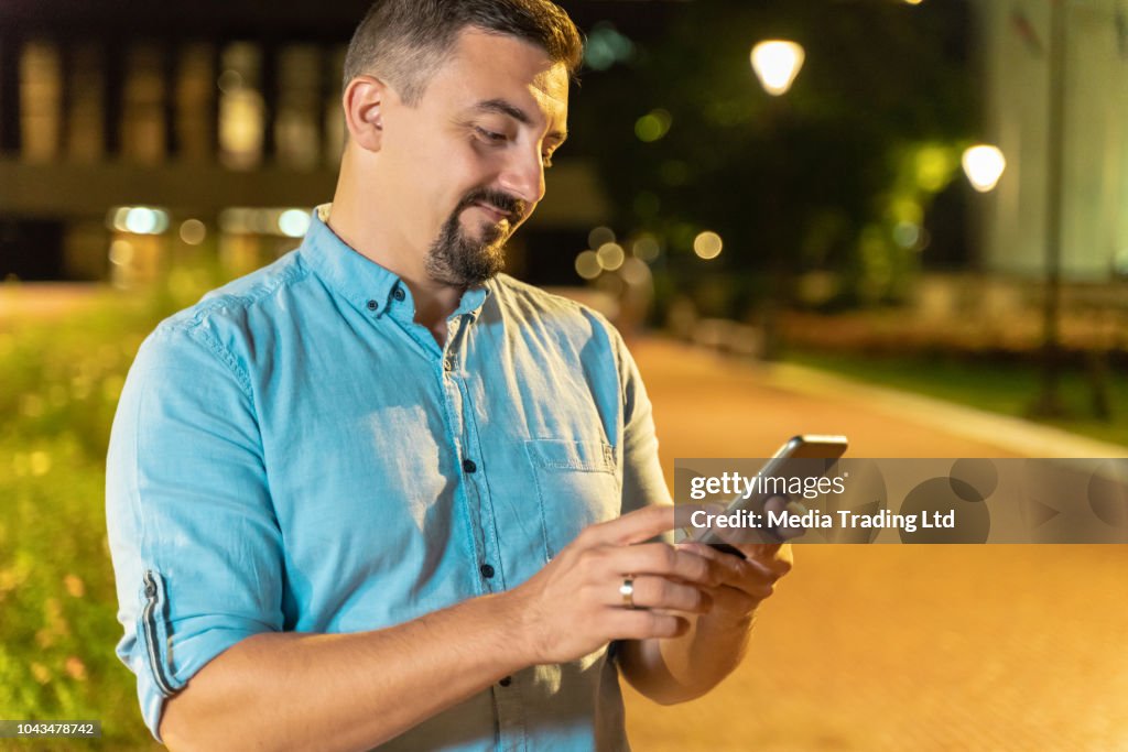 Hombre mirando su teléfono inteligente sonriendo al aire libre en la noche