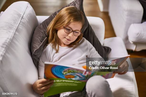 girl lying on couch at home reading booklet - workbook stock pictures, royalty-free photos & images