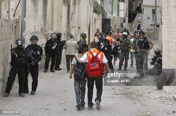 Palestinian school children walk past Israeli riot police during clashes with masked youths on September 22, 2010 after an Israeli settler guard shot...