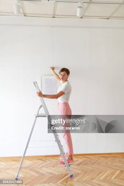 woman on the ladder hanging painting - museum curator stock pictures, royalty-free photos & images