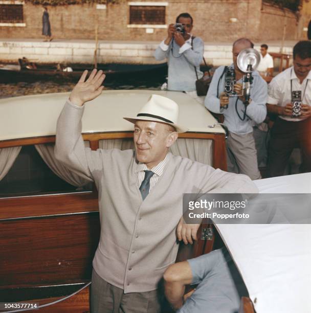 English actor Alec Guinness waves to onlookers from a boat on a canal during the 1960 Venice International Film Festival in Venice, Italy in...
