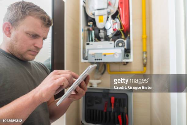 technician repairing gas furnace using digital tablet - gas appliances stock pictures, royalty-free photos & images