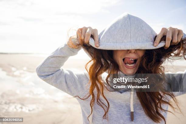 woman having fun on a windy beach, wearing hood - protection humour stock-fotos und bilder