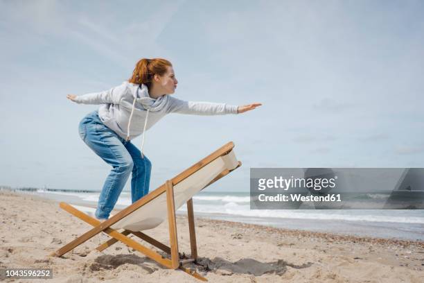 woman standing on deck chair, pretending to surf - wetterfester stuhl stock-fotos und bilder