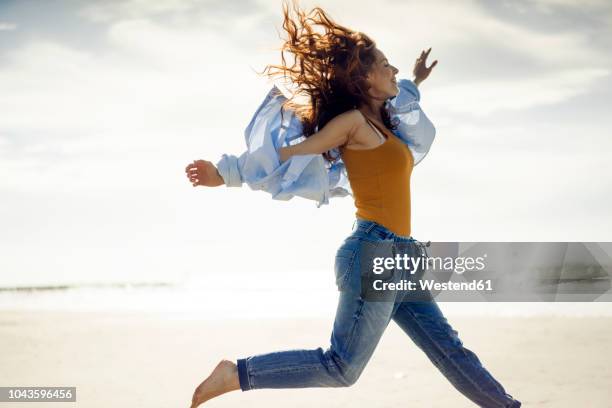 happy woman having fun at the beach, jumping in the air - running netherlands stockfoto's en -beelden